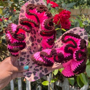 Könnte beinhalten: Handgefertigte Flip-Flops mit einem rosa und braunen Häkeldesign. Die Flip-Flops haben ein Leopardenmuster auf den Sohlen. Das Häkeldesign ist ein leuchtendes Pink mit braunen Verzierungen.
