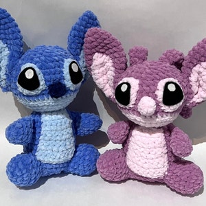 May include: Two handmade crochet plush toys. One is blue with large ears and black eyes, the other is purple with similar features. Both are sitting, showcasing their soft, textured yarn construction. The toys are inspired by a popular animated character.