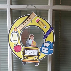 Peut inclure: Une décoration murale circulaire jaune sur le thème de l'école avec une découpe d'élève, une règle, un crayon, un crayon violet, un flacon de colle, une pomme rouge, un sac à dos bleu et un bus scolaire jaune avec le texte 2025 sur la vitre.