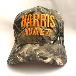 May include: A camouflage baseball cap with the text "HARRIS WALZ" embroidered in orange.