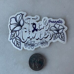May include: A white sticker with black outline and purple ribbon. The sticker says "F*ck Cancer" with the word "Pancreatic" above the word "Cancer". The sticker is decorated with two black and white flowers.