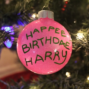 May include: Pink Christmas ornament with glitter and green lettering that reads "Happy Birthday Harry".