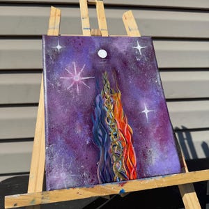 Puede incluir: Pintura abstracta sobre lienzo, exhibida en un caballete de madera. La obra presenta un fondo morado con estrellas blancas y un diseño central de formas fluidas azules, naranjas y doradas. Una luna blanca está en la parte superior.
