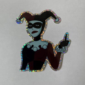 May include: A holographic sticker featuring Harley Quinn from the animated series, with a red and black jester costume, black eye mask, and a mischievous expression. She is giving the middle finger.