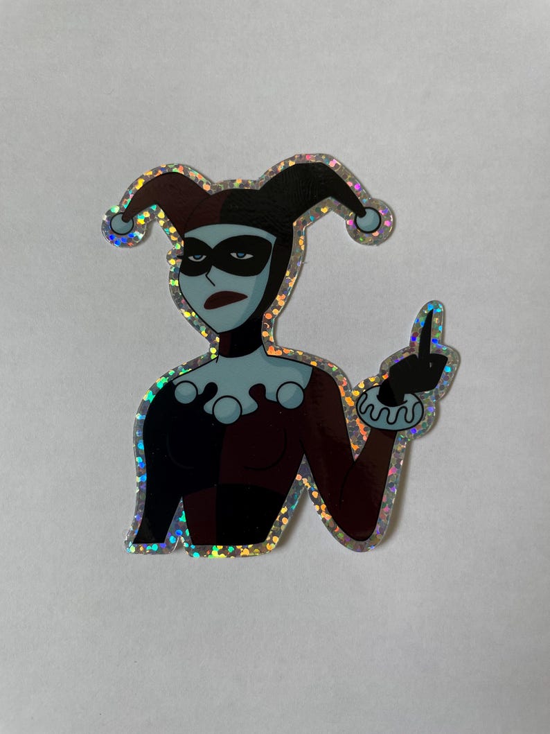 May include: A holographic sticker featuring Harley Quinn from the animated series, with a red and black jester costume, black eye mask, and a mischievous expression. She is giving the middle finger.