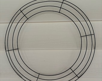 May include: A circular black wire wreath frame consisting of four concentric rings connected by perpendicular crossbars. The metal structure is designed for crafting and decorating, featuring a simple, open design that provides a sturdy base for attaching various materials to create a finished wreath.
