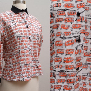 May include: A white button-down shirt with a repeating pattern of orange train cars and black accents. The shirt has a black collar and cuffs, and black buttons down the front. The long-sleeved shirt is displayed on a mannequin.