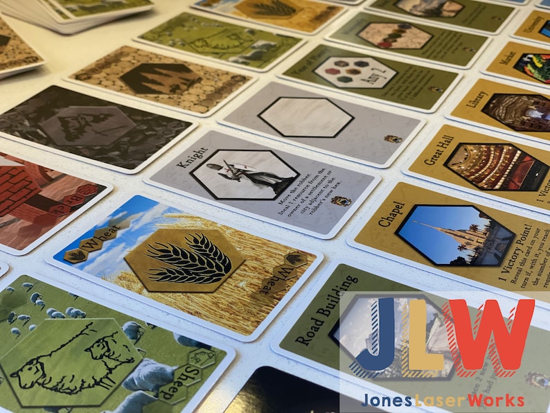 Puede incluir: Una colecci&oacute;n de cartas para un juego de mesa, con im&aacute;genes de trigo, ovejas, un caballero, una capilla, una construcci&oacute;n de carretera y un gran sal&oacute;n. Las cartas est&aacute;n sobre una superficie blanca.