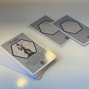 Puede incluir: Una pila de cartas de juego grises y blancas con una ilustraci&oacute;n de caballero y el texto "Knight" en la carta superior. El texto de la carta dice "Move the robber. Steal 1 resource from the owner of a settlement or city adjacent to the robber's new hex."