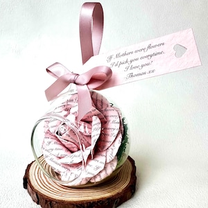 Peut inclure: Une décoration en forme de globe en verre avec une rose en papier à l'intérieur, posée sur une tranche de bois. Un ruban rose et une étiquette avec le texte "If Mothers were flowers I'd pick you everytime. I love you! Thomas xx" sont attachés.