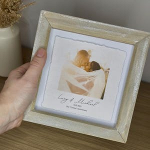 Pu&ograve; includere: Cornice quadrata in legno chiaro con una fotografia di una coppia che si abbraccia. La foto ha un tono morbido e caldo. La cornice ha una finitura invecchiata. Il testo sulla foto recita "Lucy & Michael" e "Our 'Cotton' Anniversary".