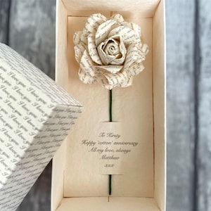 May include: A paper rose made from printed text, presented in a cream-colored box. The rose has a green stem and is accompanied by a gift box with matching text. The box includes a message: "To Kirsty, Happy 'cotton' anniversary, All my love, always, Matthew."