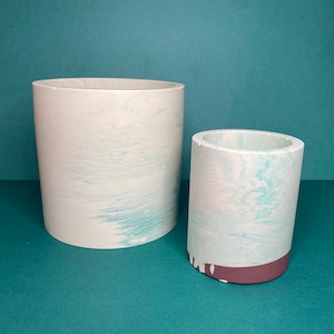 May include: Two white ceramic planters with a marbled blue and white design. The smaller planter has a brown rim.