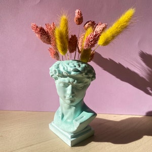 May include: A light blue plaster bust of a man with a sculpted head, used as a vase. The vase is filled with dried pink and yellow flowers.