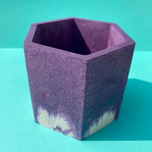 May include: A hexagonal purple planter with a textured surface and a white and purple marbled design.