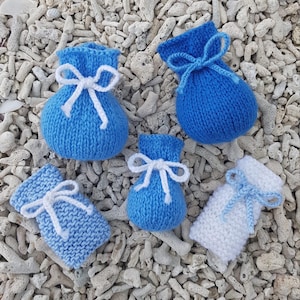 May include: An assortment of small, knitted pouches in shades of blue and white, each tied with a contrasting white or blue string. The pouches are arranged on a bed of white coral fragments, showcasing their handmade texture and design.