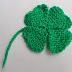 May include: A green knitted four-leaf clover with a long stem.