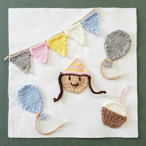 May include: A knitted felt birthday scene featuring a girl wearing a party hat, a cupcake with a candle, two balloons, and a string of flags.