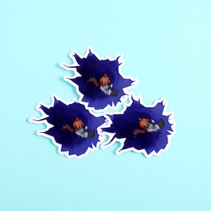 K&ouml;nnte beinhalten: Drei gestanzte Aufkleber mit einem zentralen, dunkelblauen Aquarell-Spritzer. Jeder Aufkleber zeigt eine kleine Zeichentrickfigur mit orangefarbenen Haaren und einem grau-wei&szlig; karierten Outfit in der Mitte des blauen Tintenkleckses.