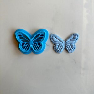 May include: Two butterfly cookie cutters, one blue and one light blue. The blue cutter is a detailed design with a cutout pattern. The light blue cutter is a solid design.