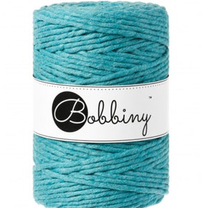 May include: A cylindrical spool of teal colored cord wrapped in a textured, braided pattern. A white paper band encircles the center of the spool, featuring the word Bobbiny printed in a black script font inside a black circular logo.
