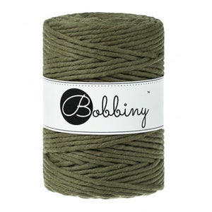 May include: A spool of olive green macrame cord. The cord is tightly wound and wrapped with a white label featuring the word "Bobbiny" in a black circle. The cord is suitable for various crafting projects.