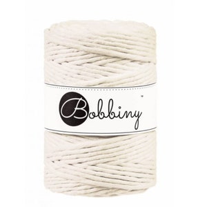 May include: A cylindrical spool of off-white cotton cord wrapped in a thick, braided texture. A white paper label encircles the center of the spool, featuring a black circular logo with the white text Bobbing in a cursive script font.