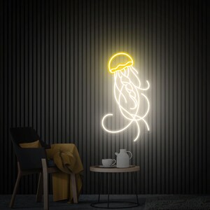 K&ouml;nnte beinhalten: Ein Neon-Schild, das eine Qualle mit einer gelben Glocke und wei&szlig;en Tentakeln darstellt. Das Schild ist an einer schwarzen Wand mit einem gestreiften Muster montiert. Im Vordergrund stehen ein Stuhl und ein kleiner Tisch mit einer Teekanne und einer Tasse.
