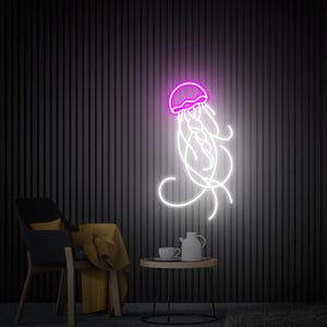 K&ouml;nnte beinhalten: Ein Neon-Schild, das eine Qualle mit einem rosa K&ouml;rper und wei&szlig;en Tentakeln darstellt. Das Schild ist an einer schwarzen Wand montiert und leuchtet, wodurch ein sanftes Leuchten entsteht.