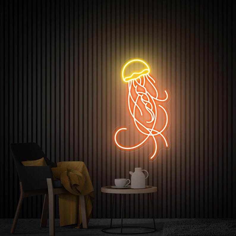 K&ouml;nnte beinhalten: Ein Neon-Schild in Form einer Qualle mit einem gelben K&ouml;rper und orangefarbenen Tentakeln. Das Schild ist an einer schwarzen Wand montiert und leuchtet.