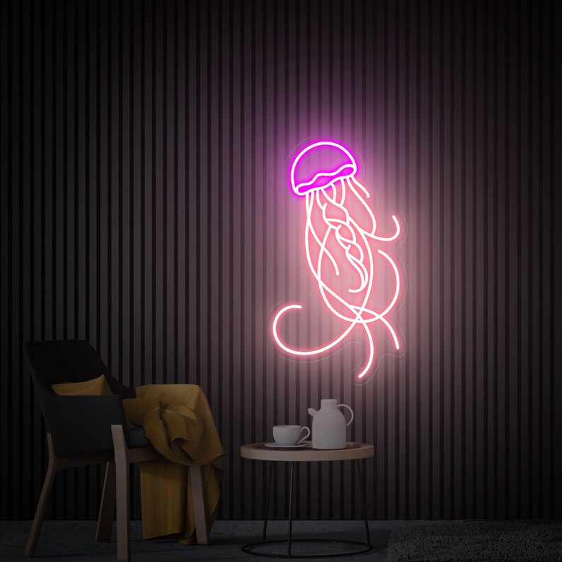 K&ouml;nnte beinhalten: Ein pinkfarbenes Neon-Schild mit einer Qualle mit wei&szlig;em Umriss. Das Schild h&auml;ngt an einer dunklen Wand mit einem Stuhl und einem Tisch davor.
