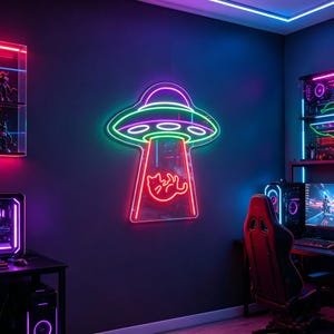 May include: A neon sign in the shape of a UFO with a cat being beamed up. The sign has a pink, green, and purple color scheme. The sign is mounted on a dark blue wall in a gaming room.