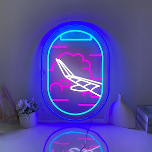 Può includere: Un cartello al neon a forma di finestrino di aereo con nuvole e un aereo che vola attraverso di esse. Il neon è blu e rosa.