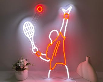 May include: White neon sign depicting a tennis player in a white outline with orange accents, holding a tennis racket and hitting a ball. The sign is lit up and has a white cord.