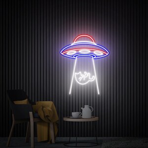 May include: A neon sign depicting a UFO in red, white, and blue, with a white beam of light shining down on a stylized baby. The sign is mounted on a dark, vertically-striped wall. A chair, table, and tea set are in the foreground.