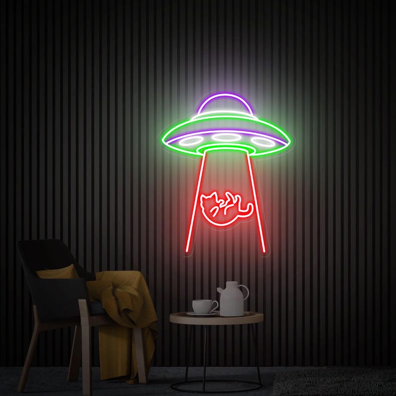 May include: A neon sign depicting a green and purple UFO with a red beam of light shining down on a cat. The sign is mounted on a dark, vertically striped wall. A black chair, a small table with a teapot and cup, and a yellow blanket are in the foreground.