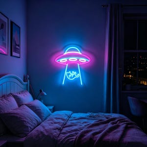 May include: A neon sign in the shape of a UFO, with a pink and blue color scheme, is mounted on a wall. The sign is above a bed with purple bedding. The room is dimly lit, with a window visible in the background.