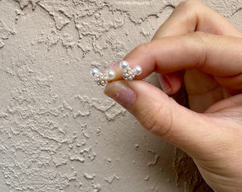 May include: A pair of pearl earrings featuring a cluster of small pearls surrounding a larger pearl in the centre. The earrings are a delicate and feminine design.