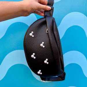 May include: A black faux leather fanny pack with a silver buckle and pearl embellishments.