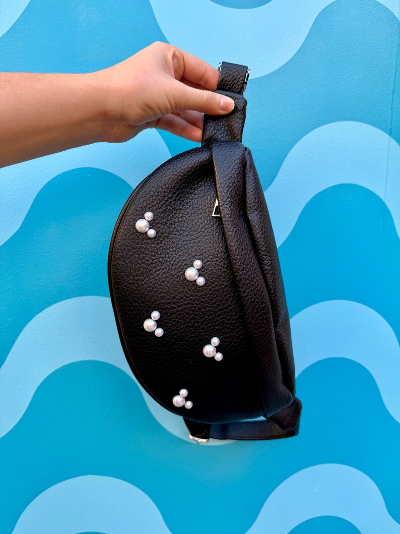 May include: A black faux leather fanny pack with a silver buckle and pearl embellishments.