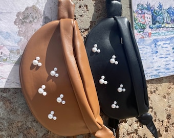 May include: Two faux leather fanny packs with pearl embellishments. The brown fanny pack has a white pearl Mickey Mouse design. The black fanny pack has a white pearl Mickey Mouse design.