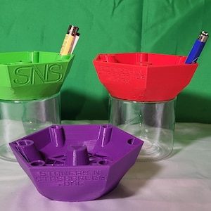 May include: Three 3D printed hexagonal containers in green, red, and purple. Each container has a small hole at the top for holding lighters or other small items. The containers are labeled "STONERS IN STASHABLES" and "SNS".