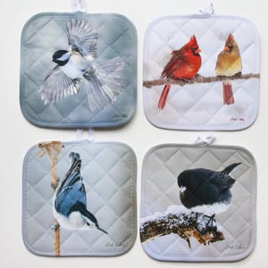 May include: Set of four quilted pot holders featuring winter birds. The pot holders are white with a quilted pattern and feature a black-capped chickadee, a cardinal, a nuthatch, and a dark-eyed junco.