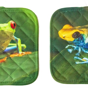 May include: Set of two green quilted pot holders with a frog design. One pot holder features a green tree frog with red eyes and the other features a yellow and blue poison dart frog.