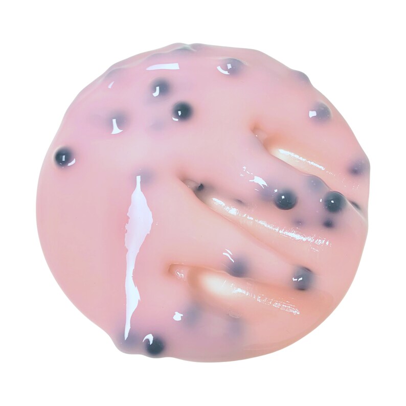 May include: A close-up of a pink and white jelly-like substance with small black seeds throughout. The substance is spread out in a circular shape.