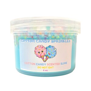 Könnte beinhalten: Ein durchsichtiger Plastikbehälter gefüllt mit blauem Schleim mit bunten Streuseln. Der Behälter hat ein weißes Etikett mit der Aufschrift "Cotton Candy Sprinkles" und "Cotton Candy Scented Slime Do Not Eat 6 oz.".