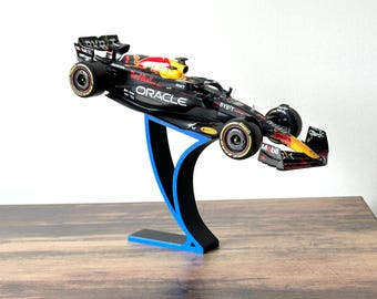 May include: A black and red Formula 1 race car model on a blue and black display stand. The car has the logos "Red Bull", "Oracle", "Bybit", and "Mobil" on it.