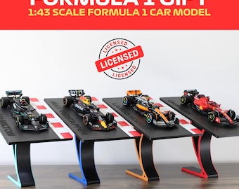 May include: Four 1:43 scale Formula 1 car models on display stands. The cars are black, orange, red, and black with orange accents. Each stand has a black base with a red and white checkered pattern and a black, blue, orange, or red stand.