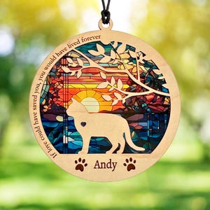 May include: A circular wooden ornament featuring a stained-glass style sunset background with a silhouette of a cat. The text reads, "If love could have saved you, you would have lived forever" and "Andy" with two paw prints.