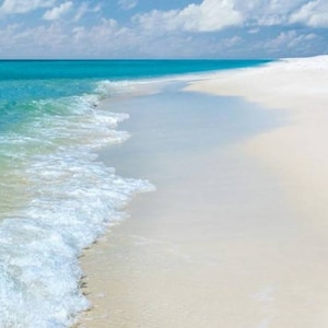 Puede incluir: Una playa de arena blanca con agua azul turquesa y olas espumosas rompiendo en la orilla.